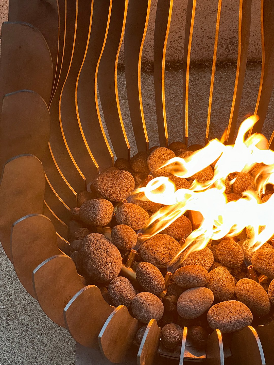 Close-up of Kelray sculptural firepit with flames dancing over natural lava rocks inside a corten steel structure.